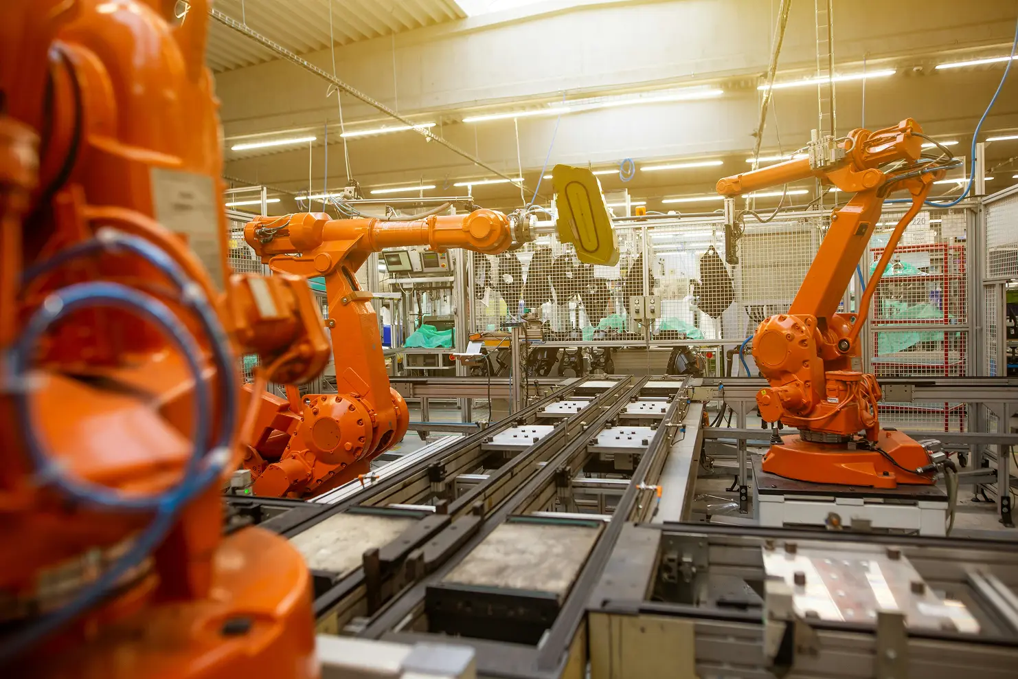 3 robotic arms working in a manufacturing factory. The arms are all orange and are not currently undertaking any tasks.