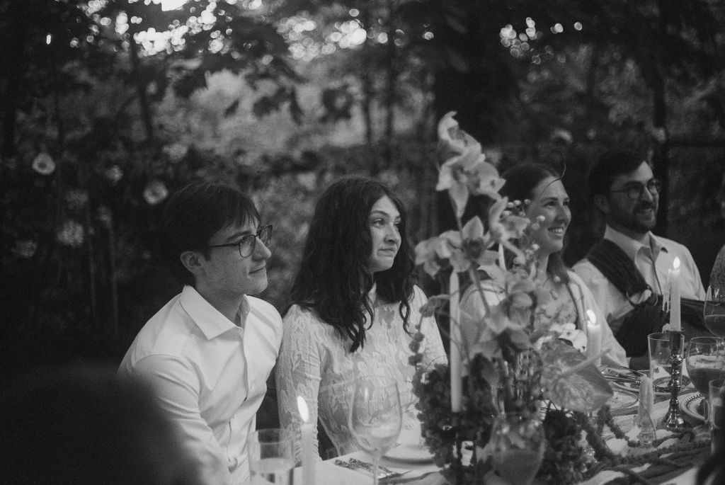 Black and white photo of four people sitting at a candlelit dinner table with floral centerpieces, engaged and smiling.