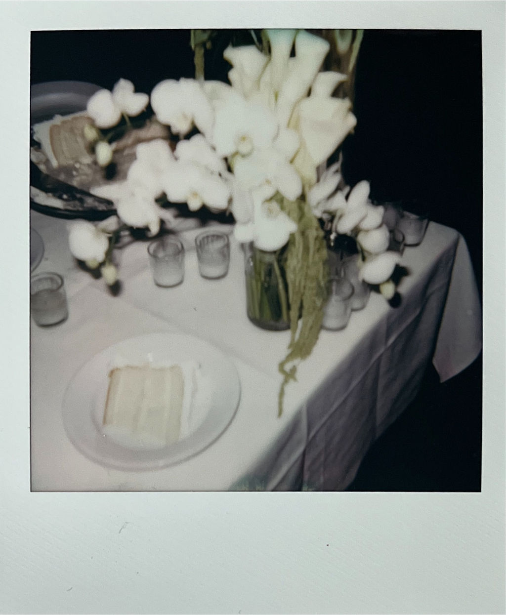 White floral arrangement in a vase on a table with a slice of layered cake on a plate nearby.