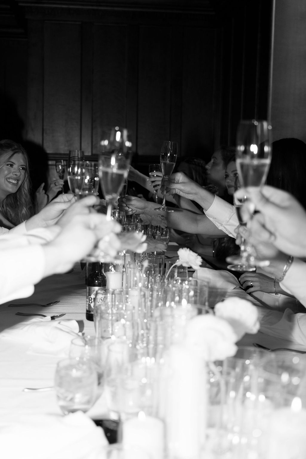 Black and white photo of a group raising champagne glasses in a celebratory toast at a dining table.