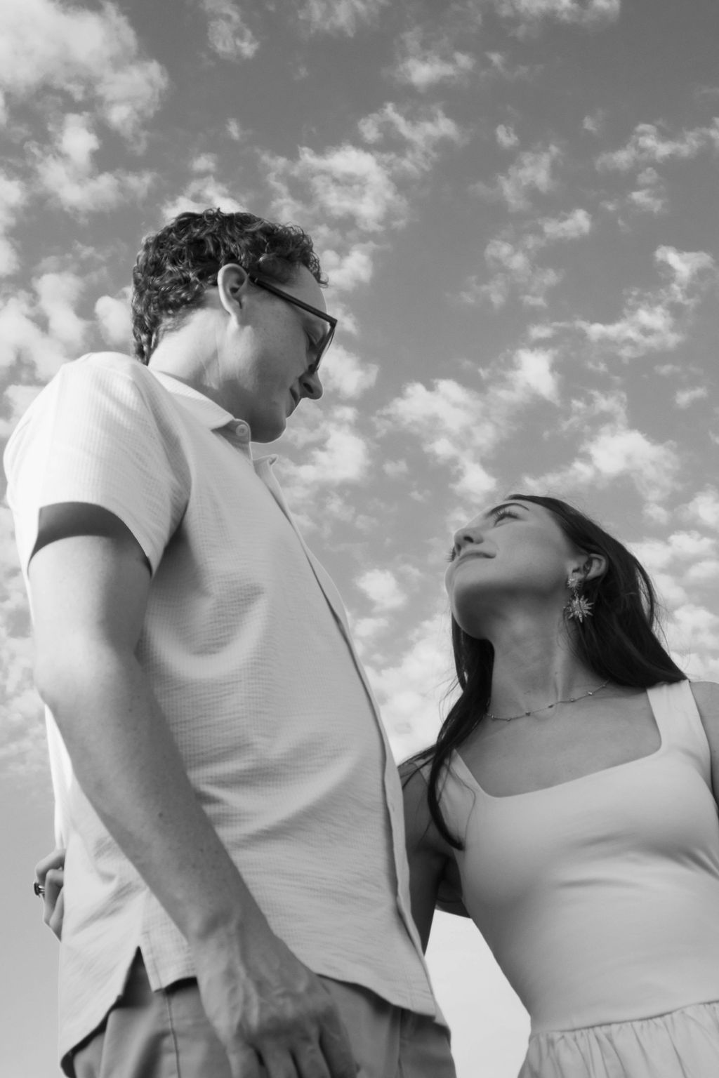 Black and white photo of a man and woman looking lovingly at each other under a cloudy sky.