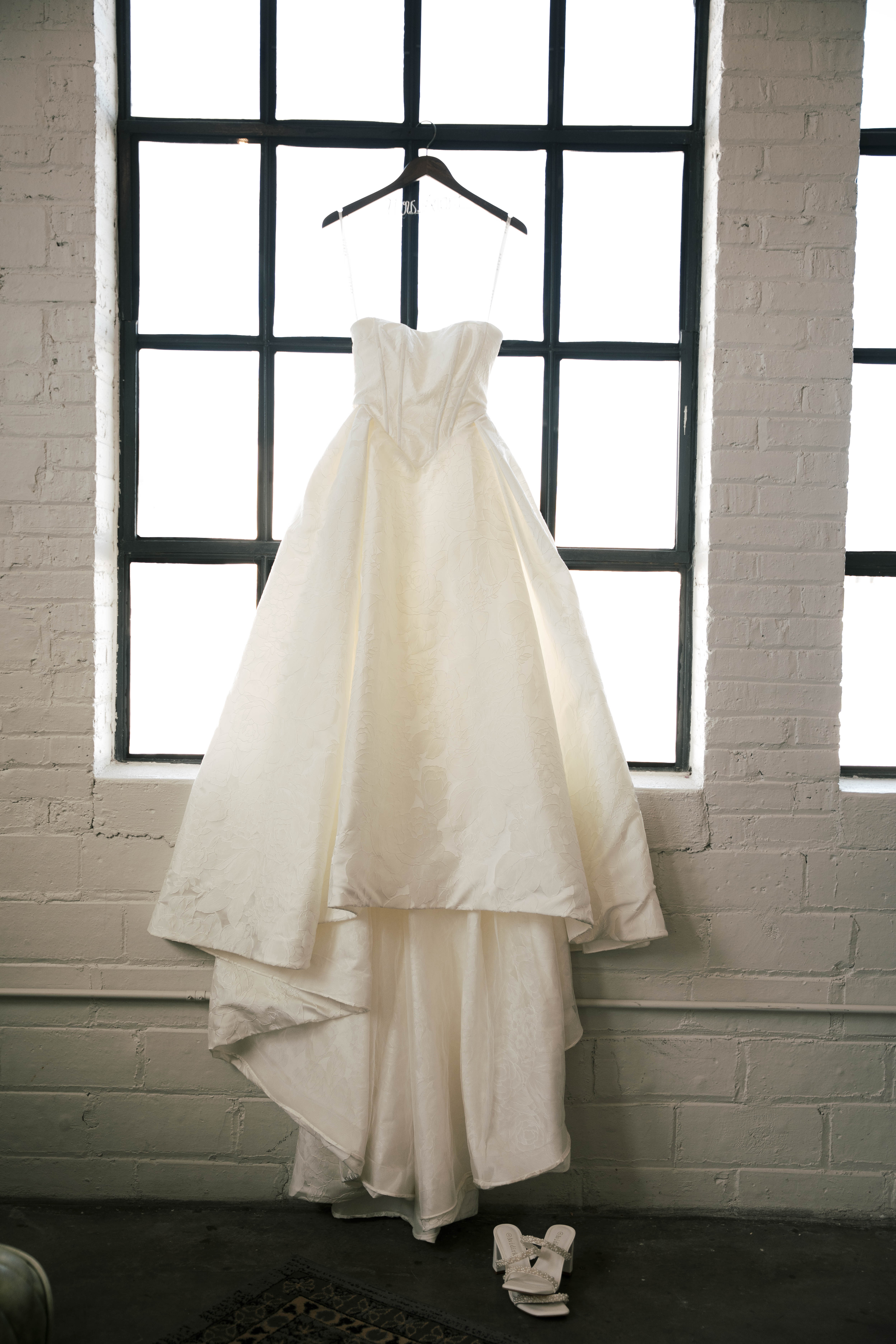 Young girl in a white dress and veil standing in profile inside a dimly lit room near a woman in a floral dress.