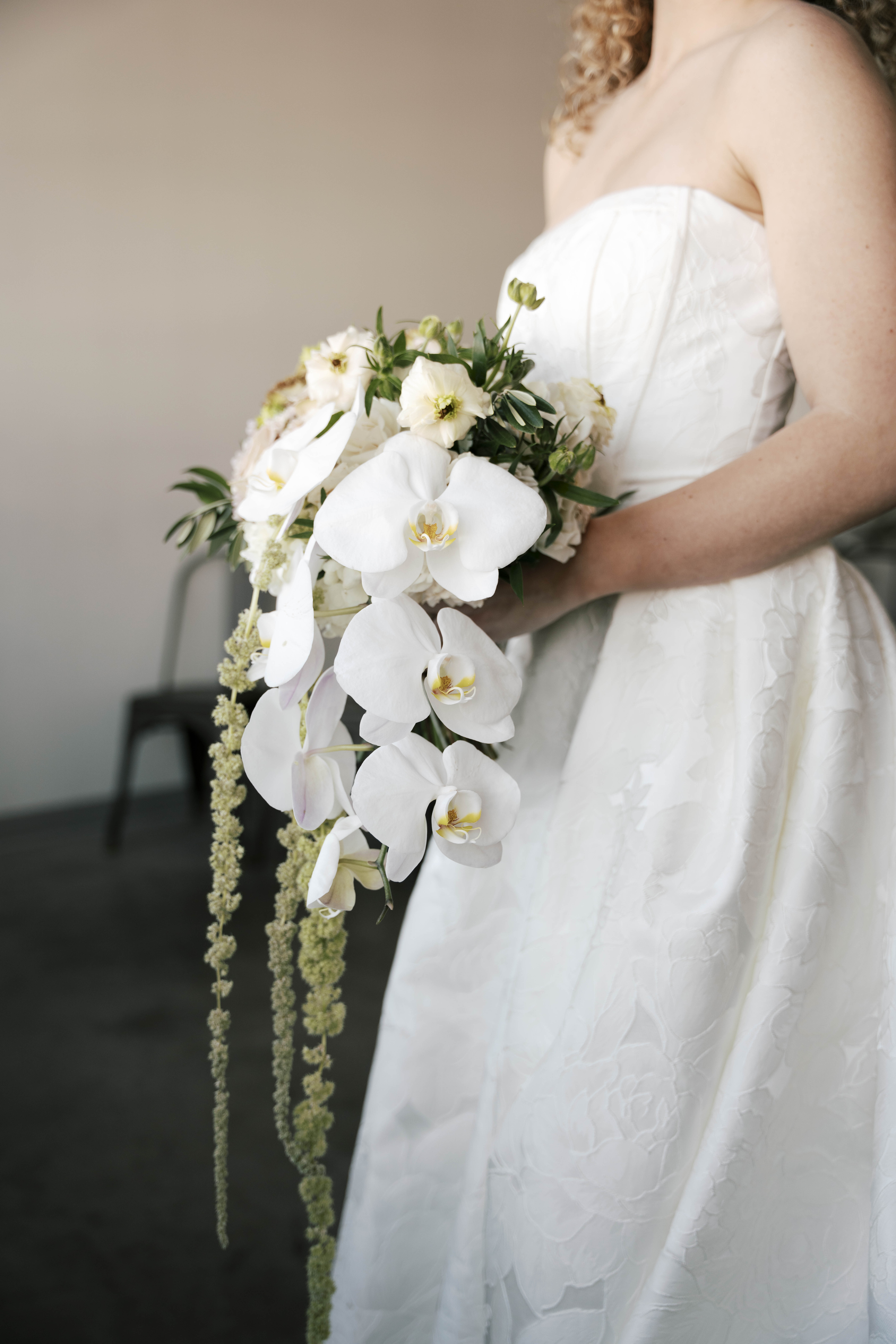 Couple dressed formally holding hands and standing apart, looking in opposite directions in front of a brick building with a white garage door.