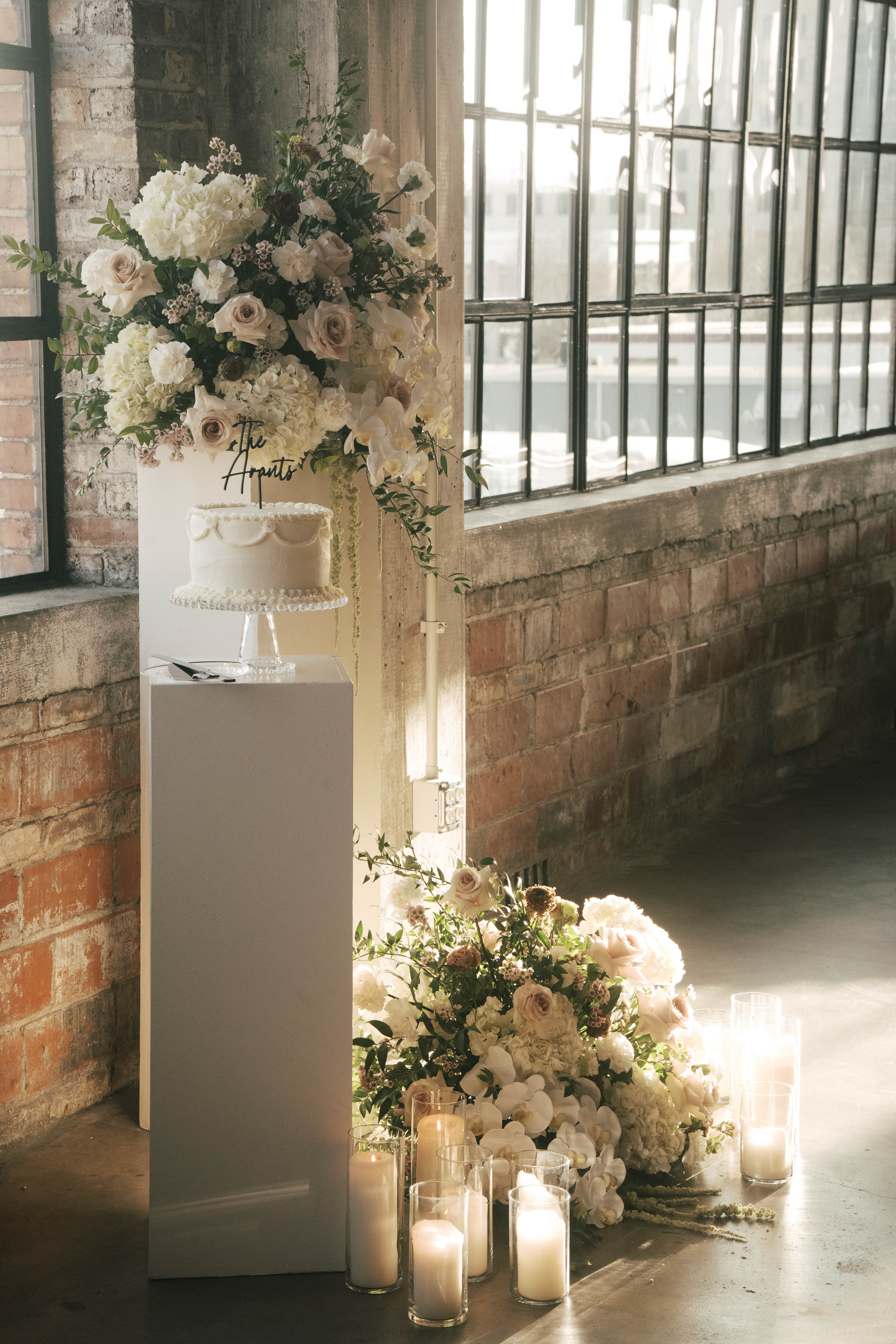 Man in a black suit and bow tie and woman in a white lace dress and green heels holding hands, leaning against a large stone pillar.