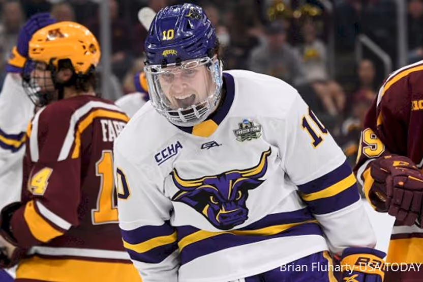 Ice hockey player in white jersey with bull logo celebrating on the ice with opposing players in maroon and yellow jerseys.
