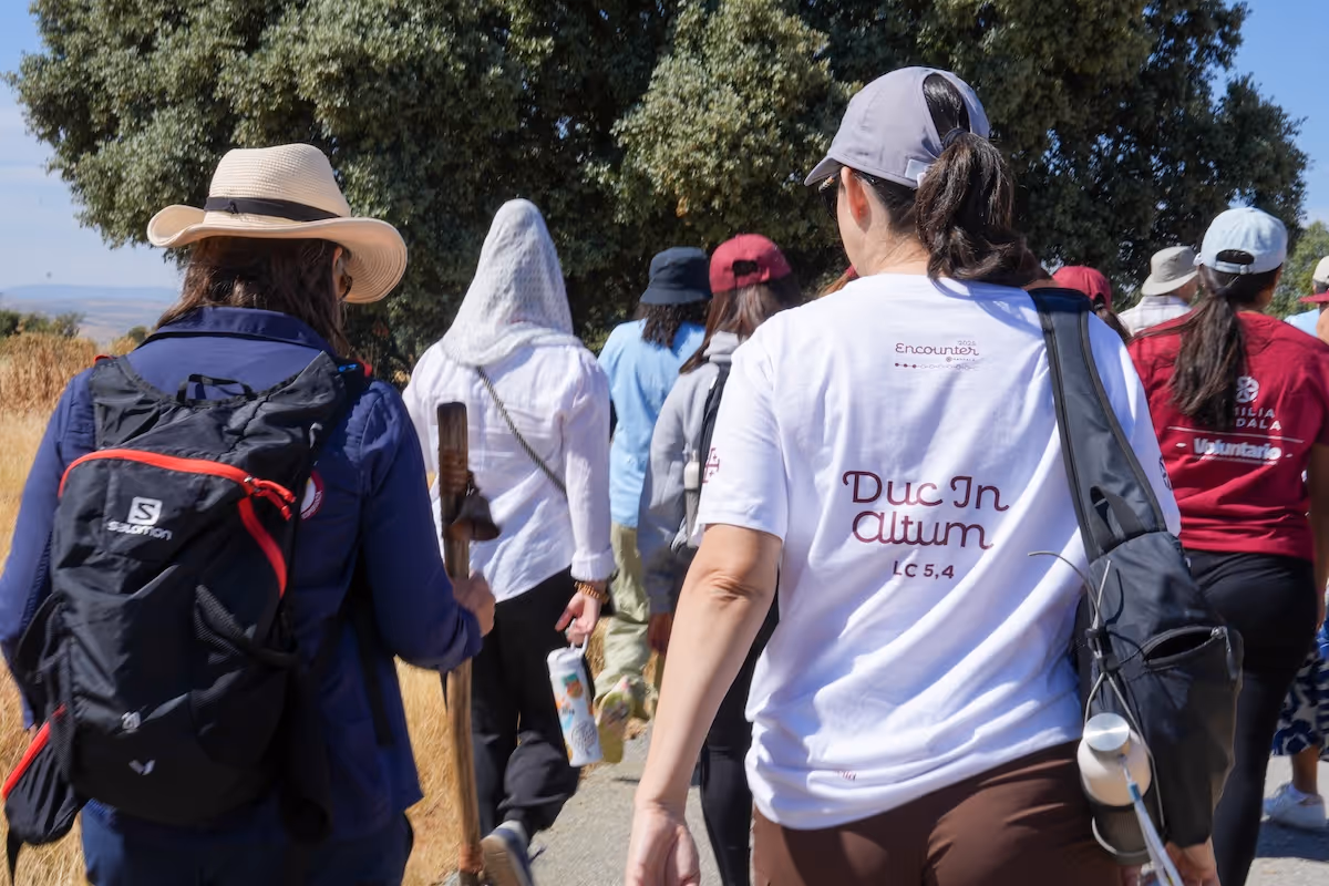 Grupo de personas caminando por un sendero al aire libre, algunas con gorras y mochilas, en un día soleado.