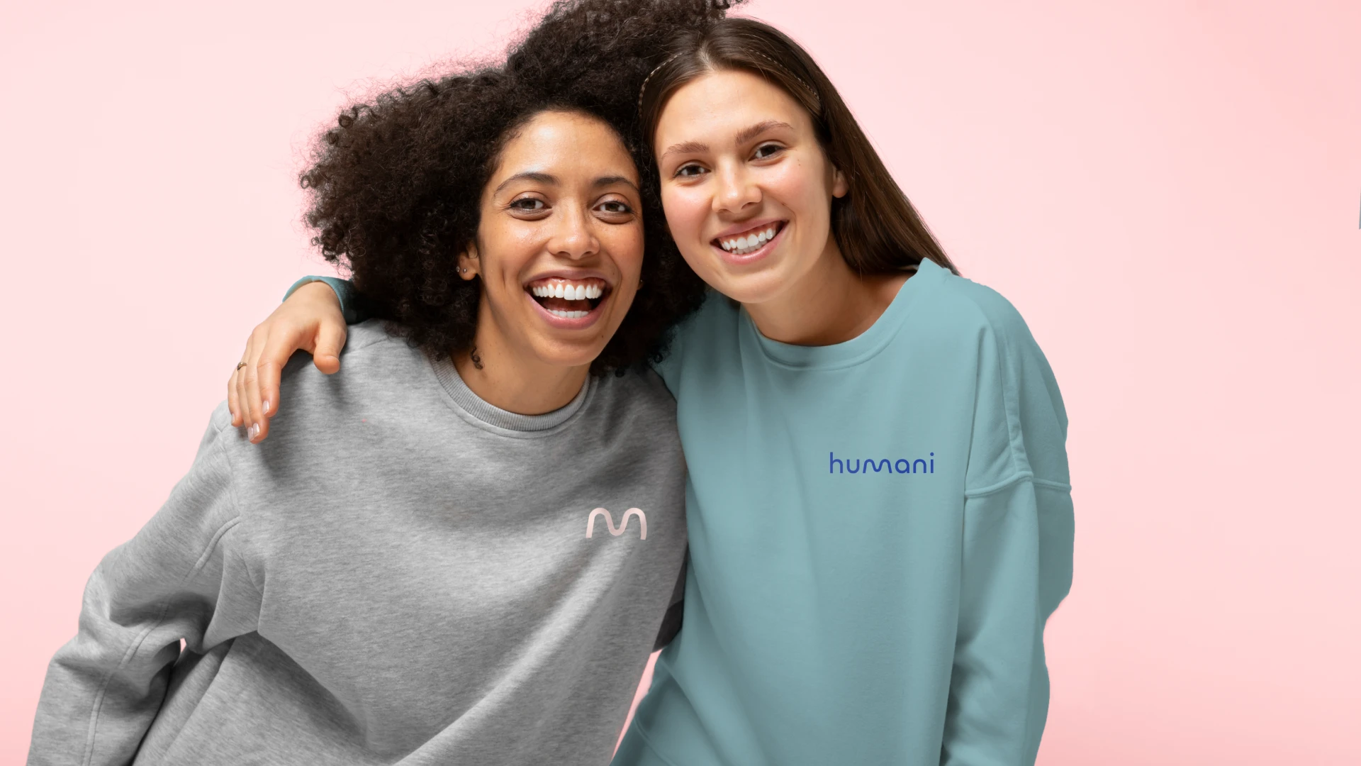 Two women leaning on each other wearing Humani hoodies