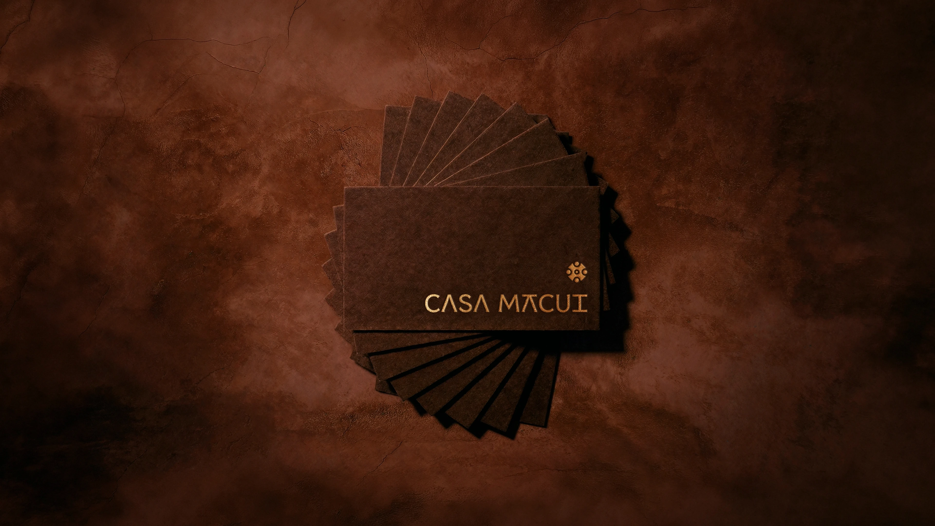 A circular fan of dark brown business cards with "CASA MACUI" in gold, centered on a textured image.