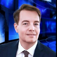Portrait of a man in a suit and tie with a blurred blue news studio background.