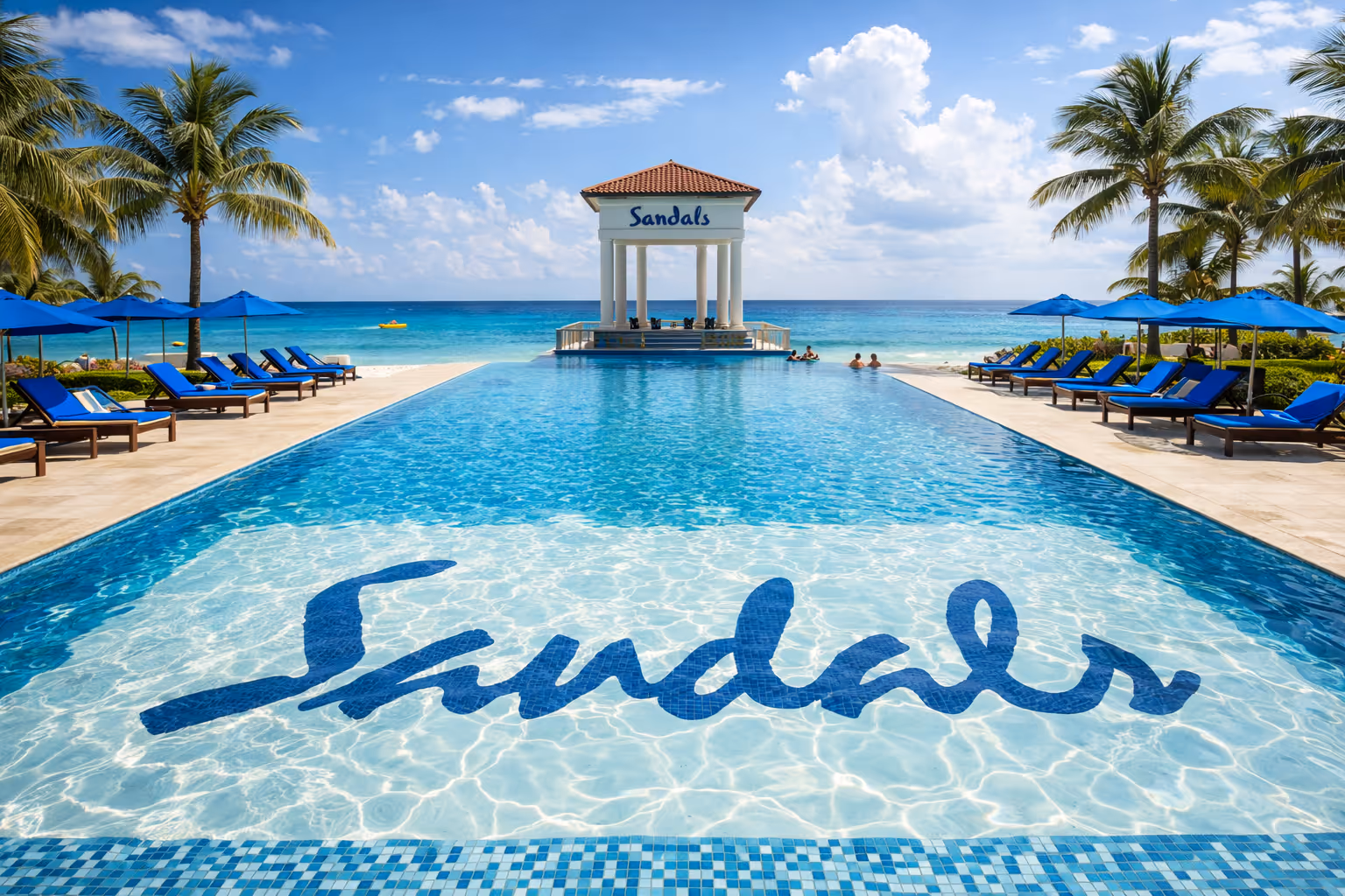 Infinity pool at a Sandals Resort overlooking the ocean with palm trees and resort buildings
