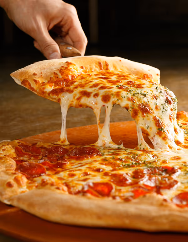 Hand lifting a slice of hot pepperoni pizza with melted, stretchy cheese.