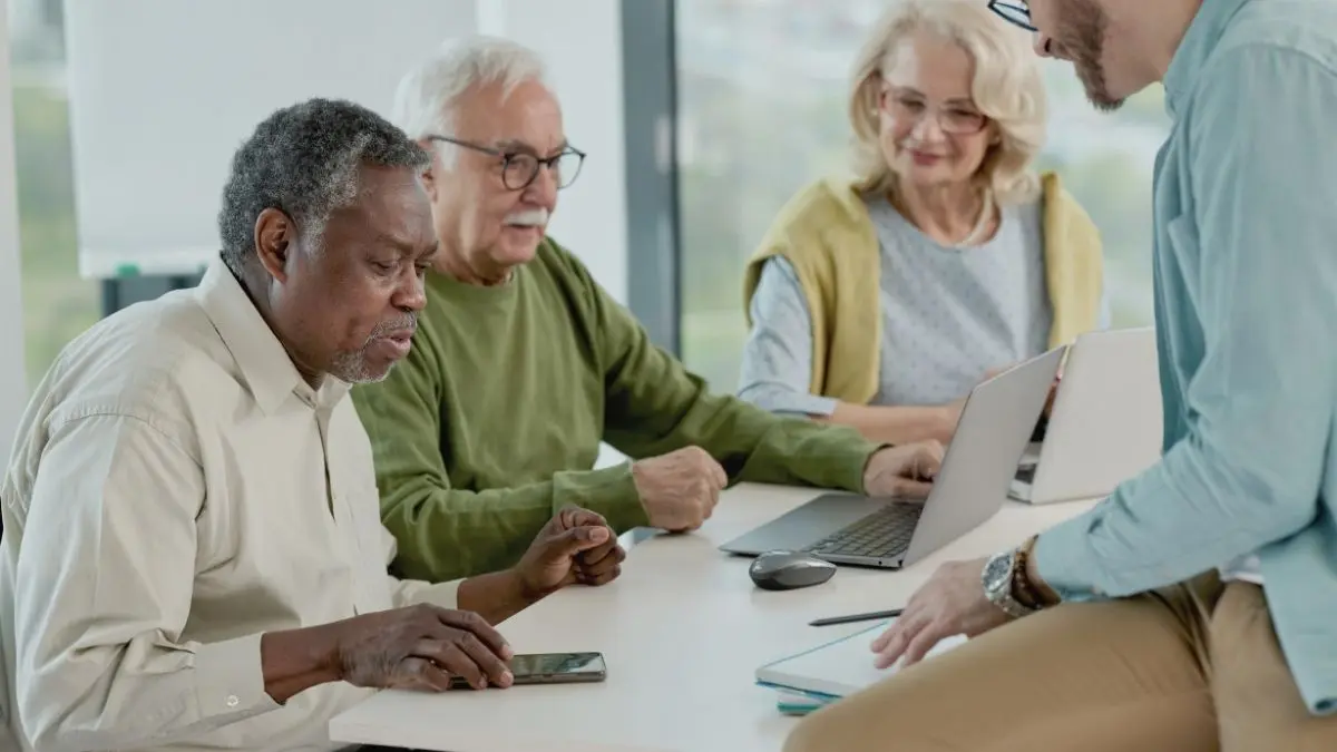 Formation en compétences numériques pour personnes de 55 ans et plus participant à un atelier pratique avec ordinateur portable et téléphone intelligent.