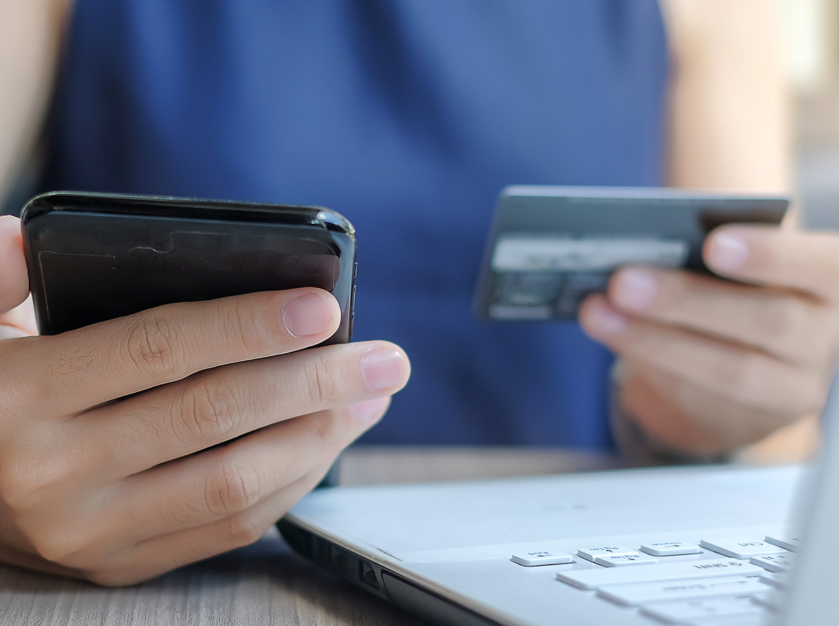 Person holding a credit card and smartphone near a laptop, making an online payment.