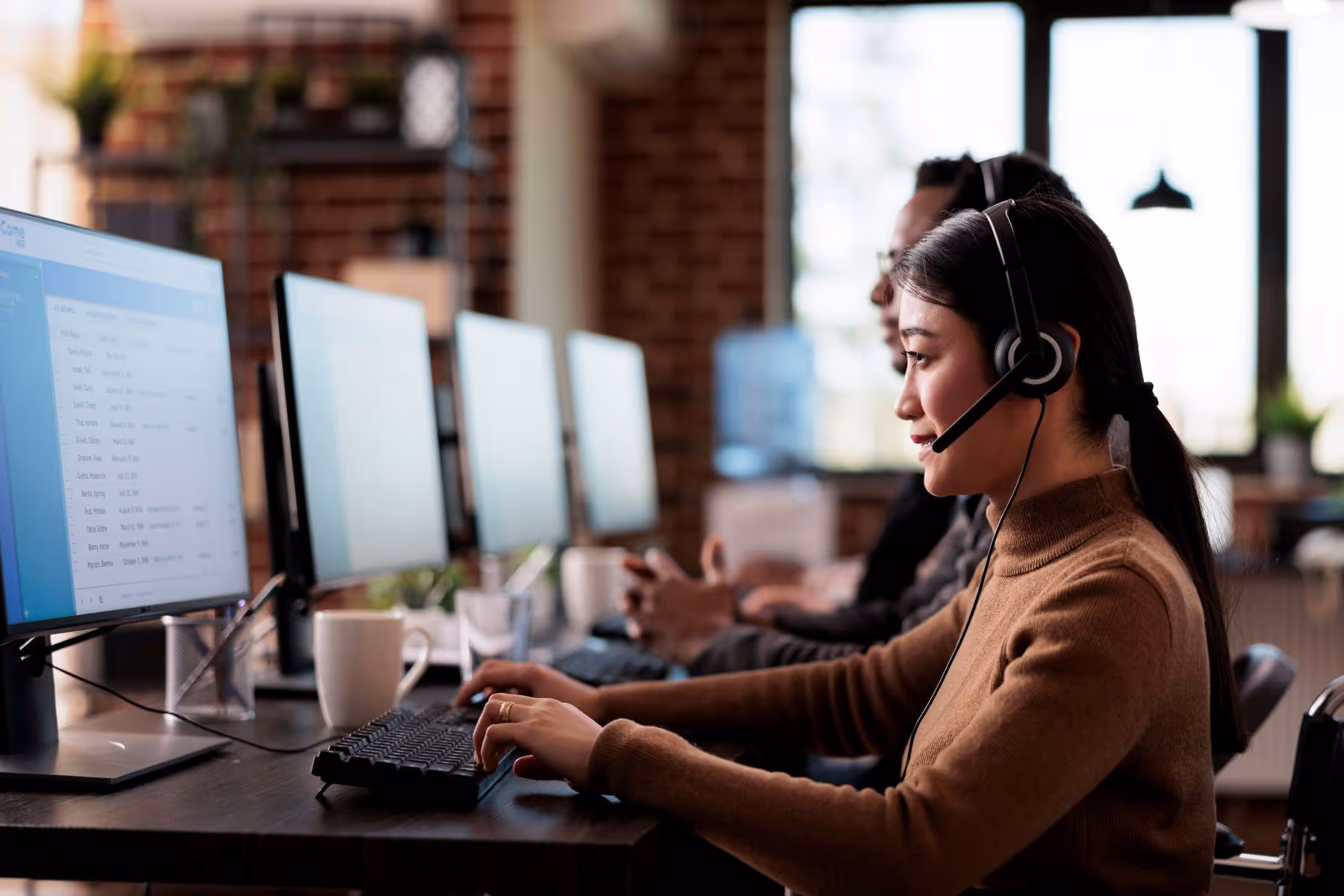 Call center receptionist with headset on while typing on keyboard and looking at computer screen