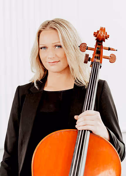Portrait of Erin Tinney wearing a black blazer and top, holding a cello upright, with blonde hair and a calm expression against a bright white background.