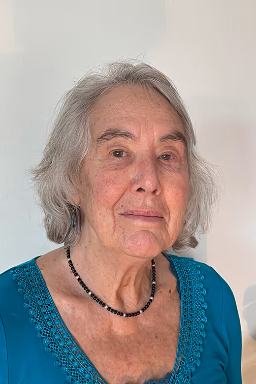 Portrait of Hazel Lennox, Director of the Comox Valley Youth Music Centre, looking calmly at the camera, wearing a teal top and a beaded necklace against a light neutral wall.