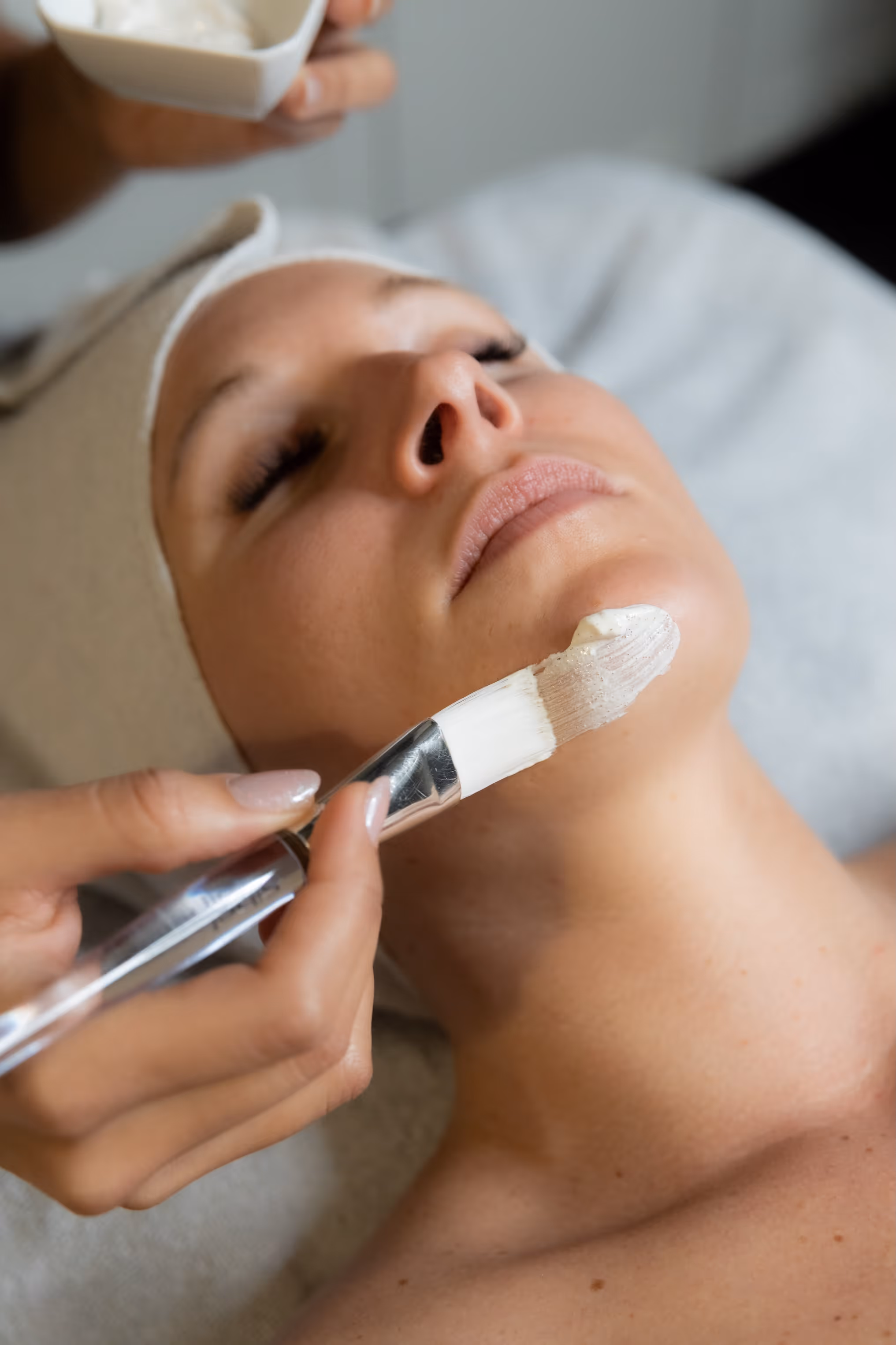 Esthéticienne appliquant un masque de soin purifiant au pinceau sur le visage d'une cliente détendue en institut.