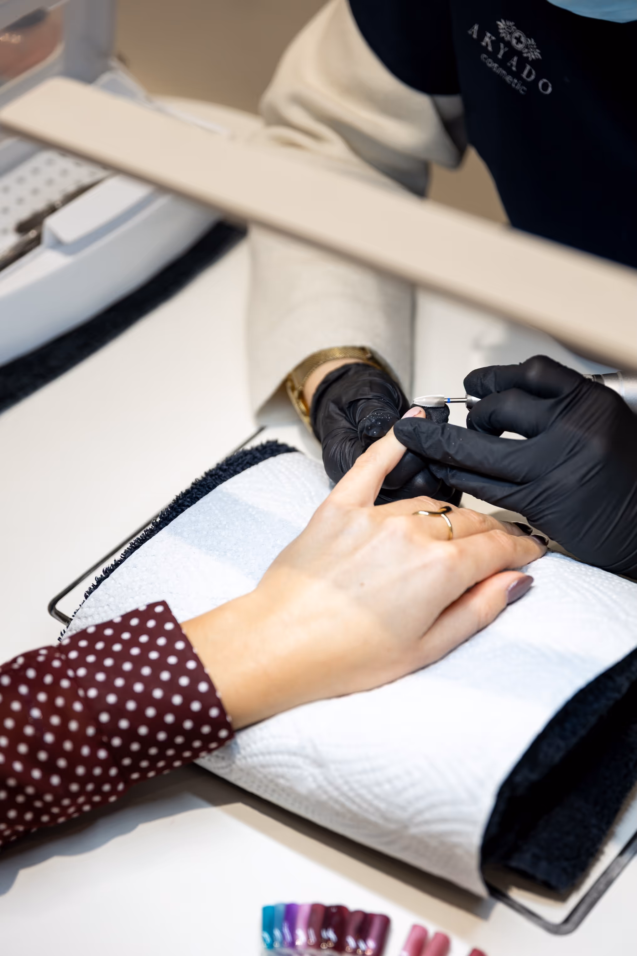 Esthéticienne utilisant une ponceuse à ongles électrique sur la main d'une cliente lors d'une prestation de manucure professionnelle en institut.