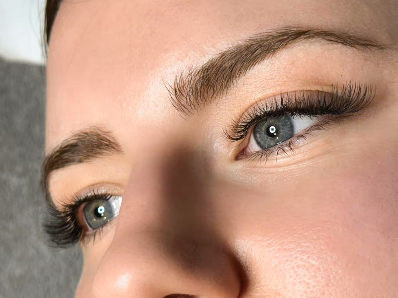 Gros plan sur le regard d'une femme mettant en valeur une extension de cils volumineuse et des sourcils parfaitement dessinés.