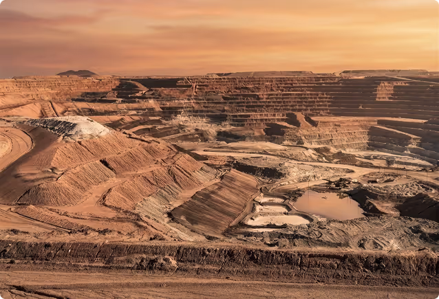Large open-pit mine with terraced excavation under a pinkish sunset sky.