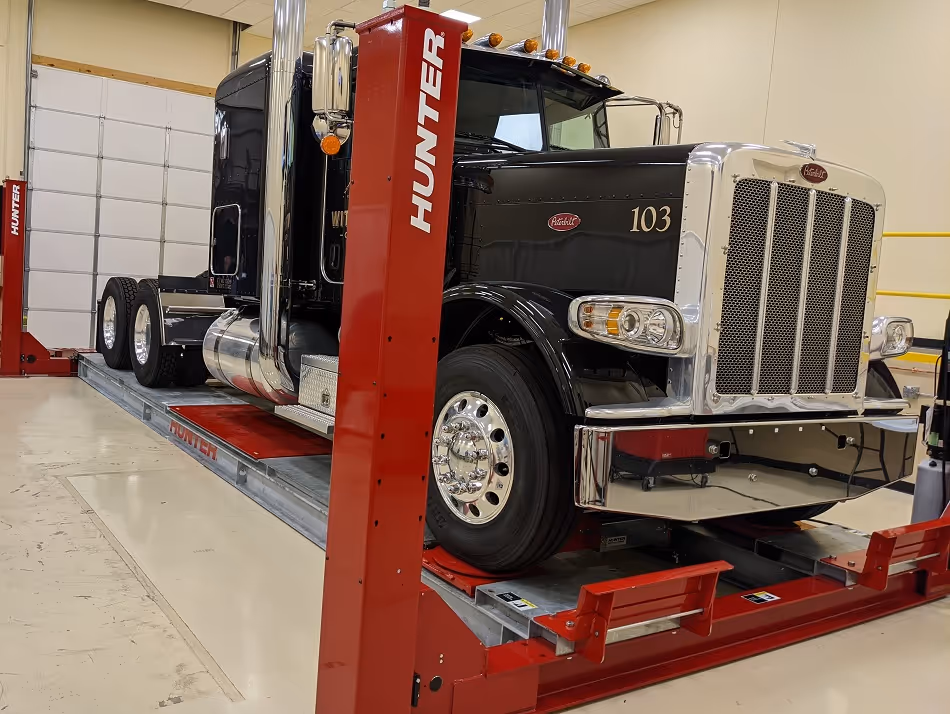 Large black Peterbilt semi-truck with number 103 on the side, positioned on a red Hunter vehicle lift inside a garage.