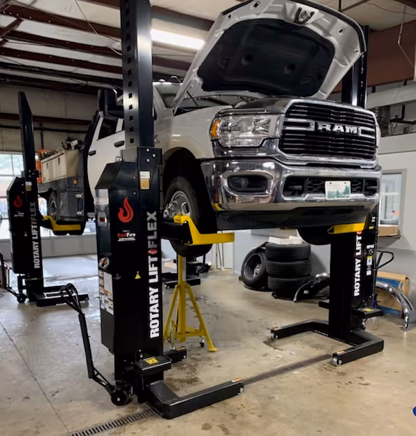 White Ram pickup truck lifted on a Rotary Lift Flex two-post car lift inside an auto repair garage.