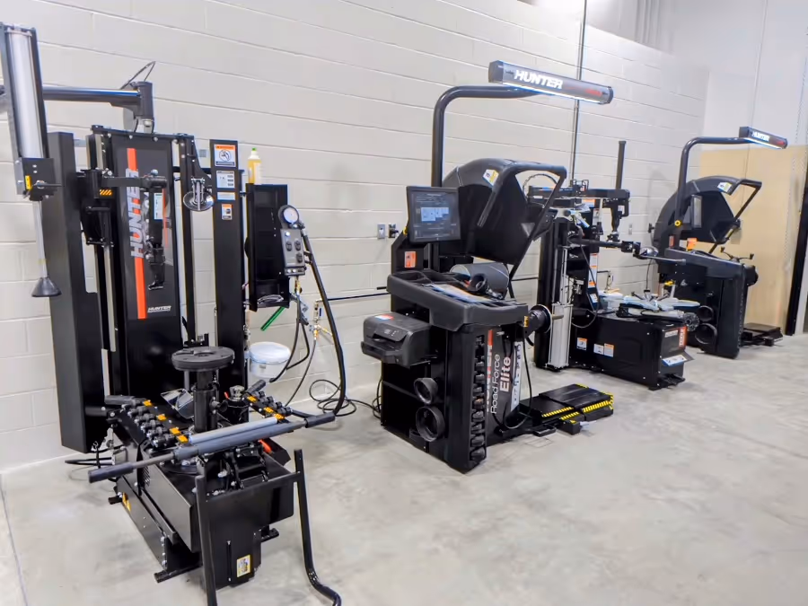 Three black Hunter automotive wheel alignment machines lined up in a workshop with concrete floor and light-colored walls.