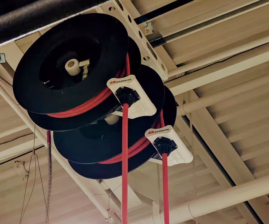 Two black hose reels mounted on a ceiling with red hoses extending downward, branded with the name Samson.