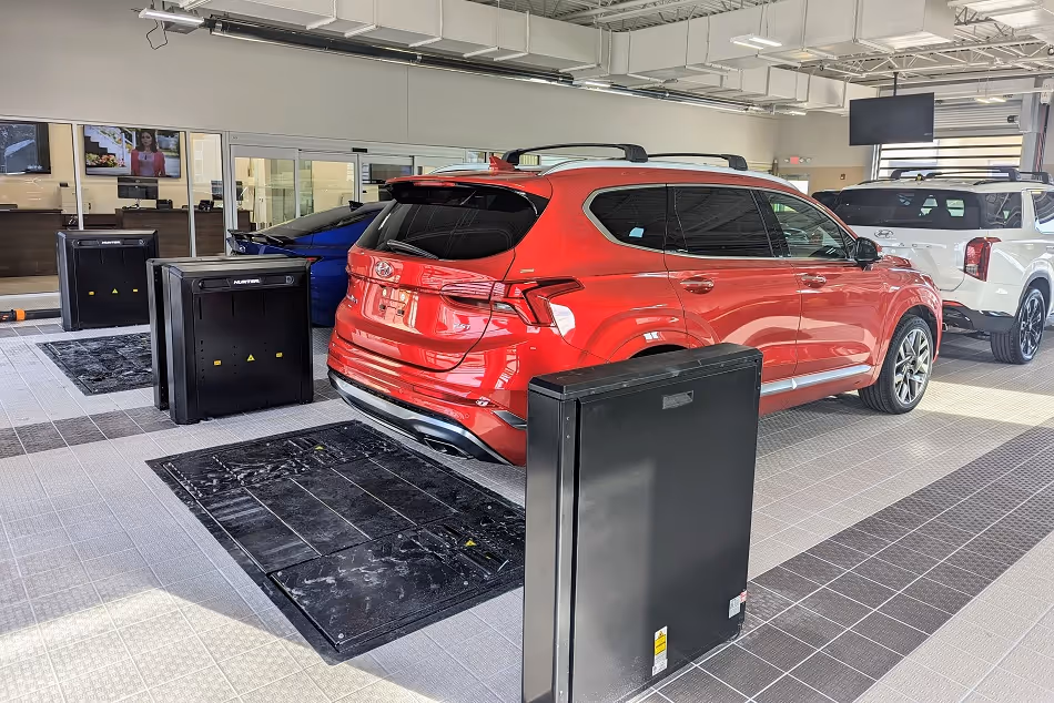 Red SUV parked inside a showroom with black battery storage units nearby and other vehicles in the background.