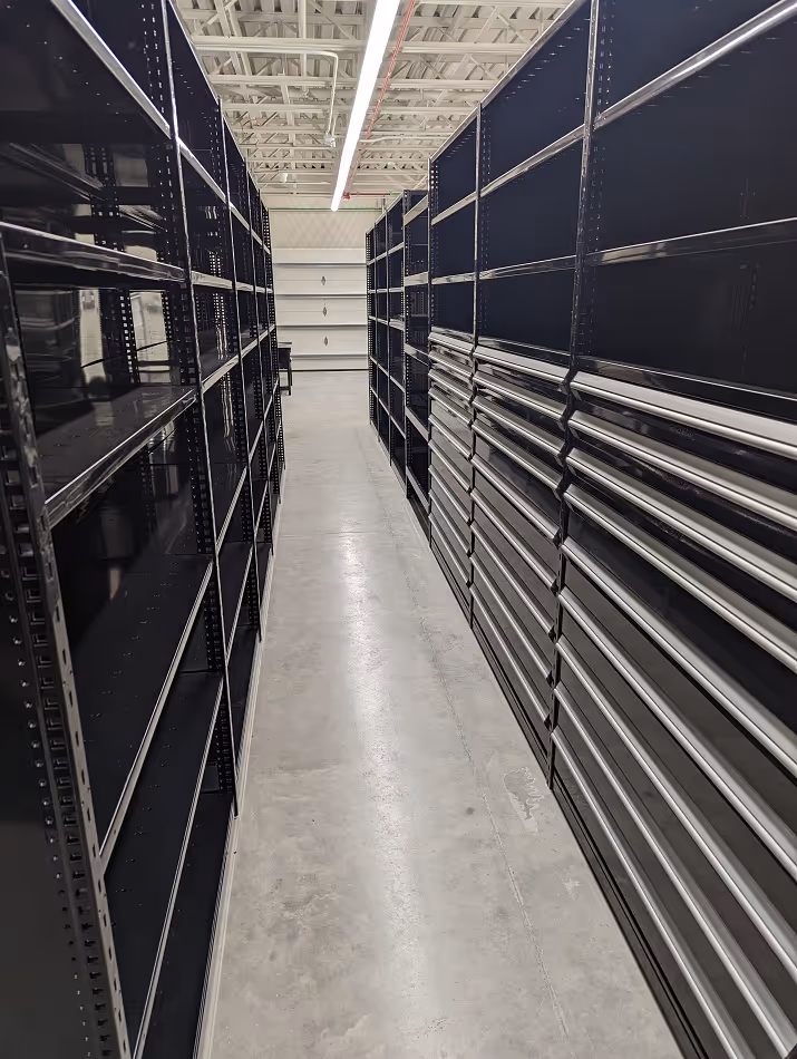 Empty metal shelves and drawers lining both sides of a concrete aisle in a well-lit industrial storage space.
