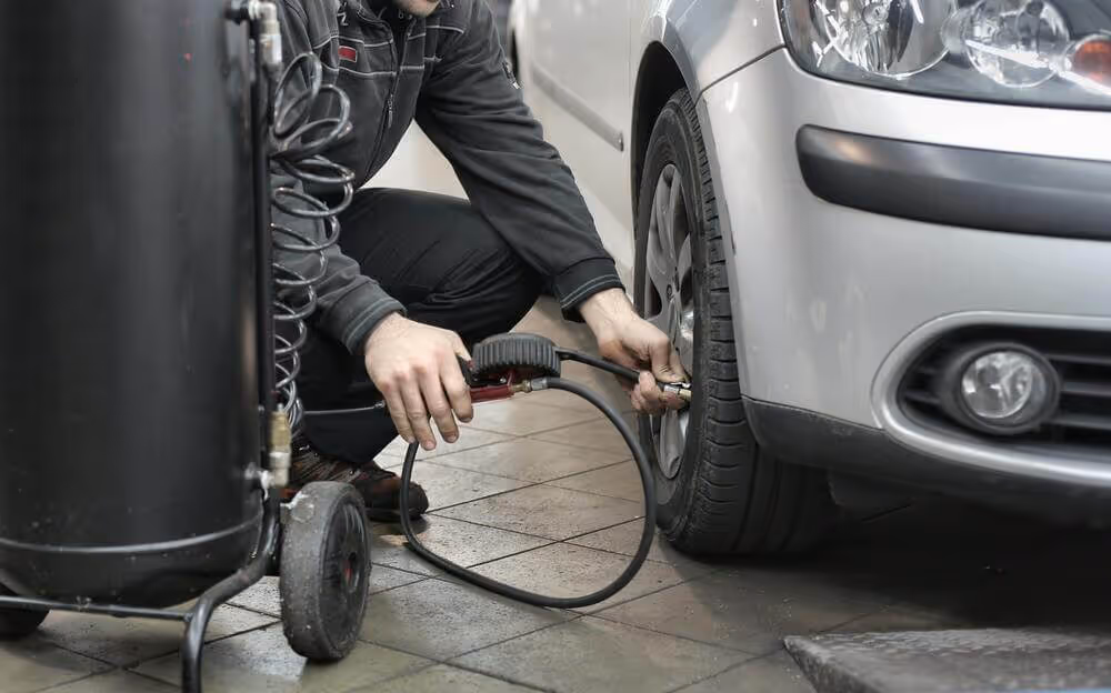 Man inflating a car tire using an air compressor in a garage.