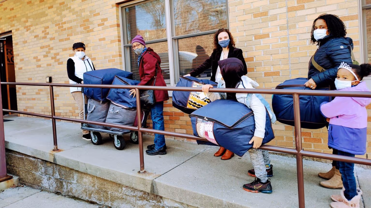 A group of adult and youth volunteers carry handmade items up a ramp to donate them