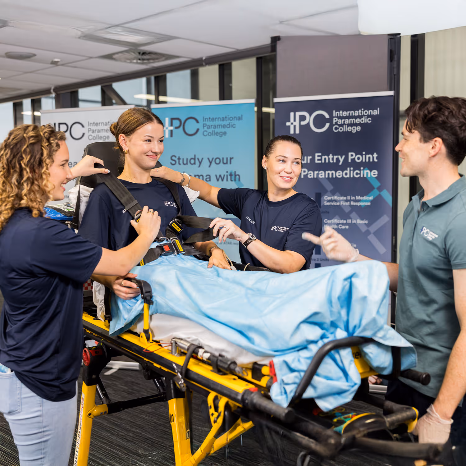 Three paramedic students securing a woman on a stretcher during training at International Paramedic College.