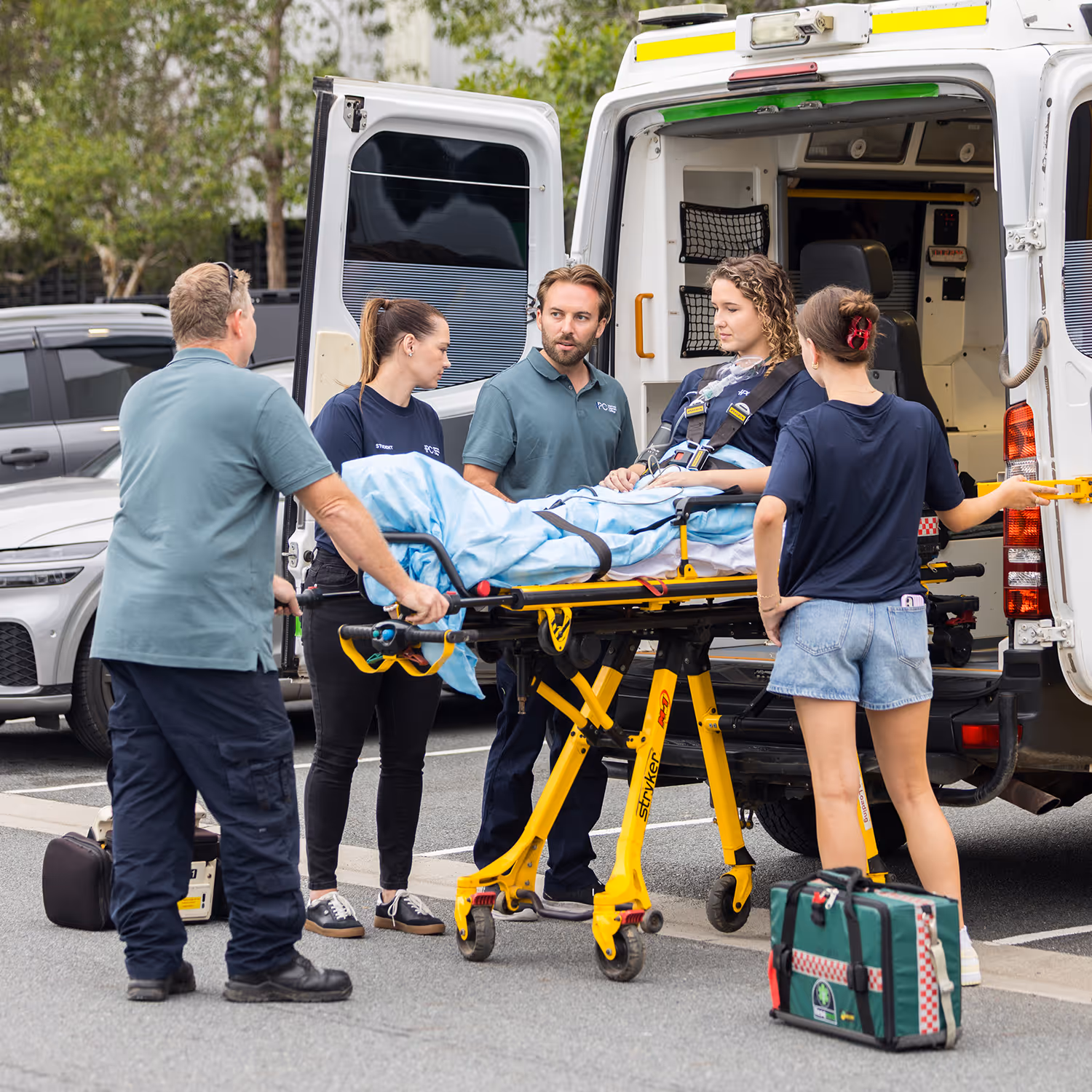 Paramedics loading a patient on a stretcher into an ambulance in a parking lot.