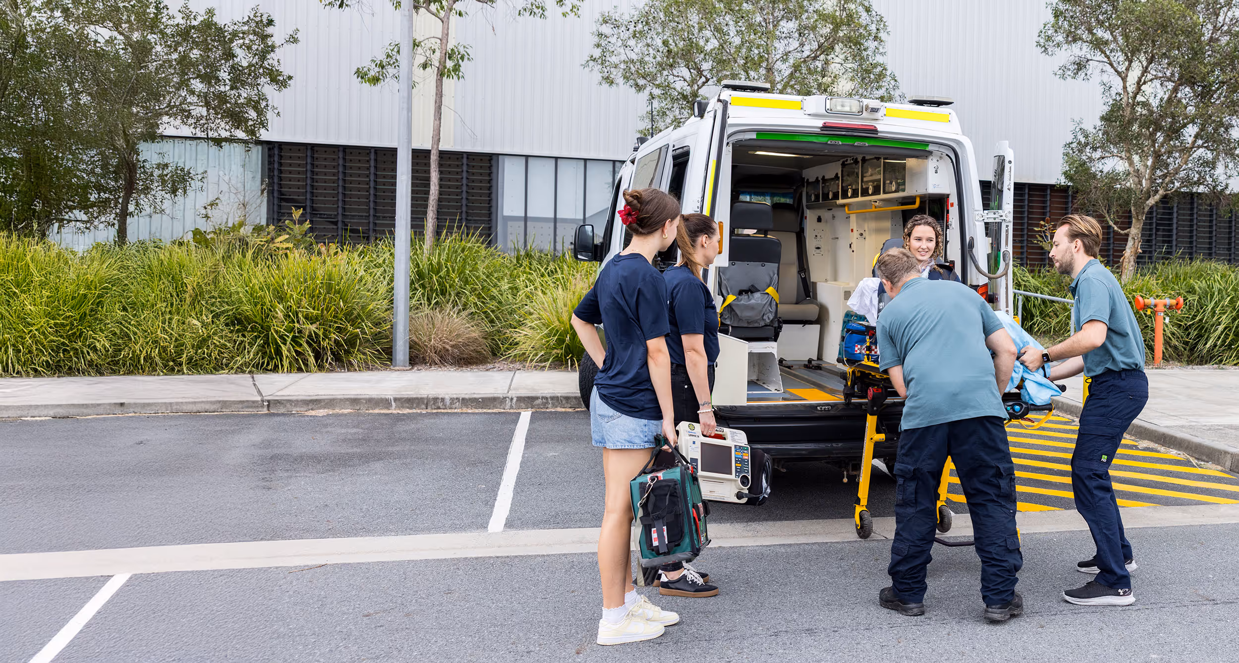 Four paramedics attending to a patient on a stretcher being loaded into an ambulance with medical equipment.