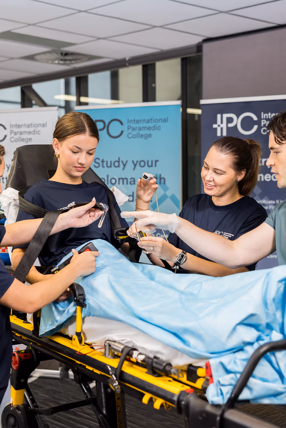 Paramedic students practicing patient care on a stretcher during training at International Paramedic College.