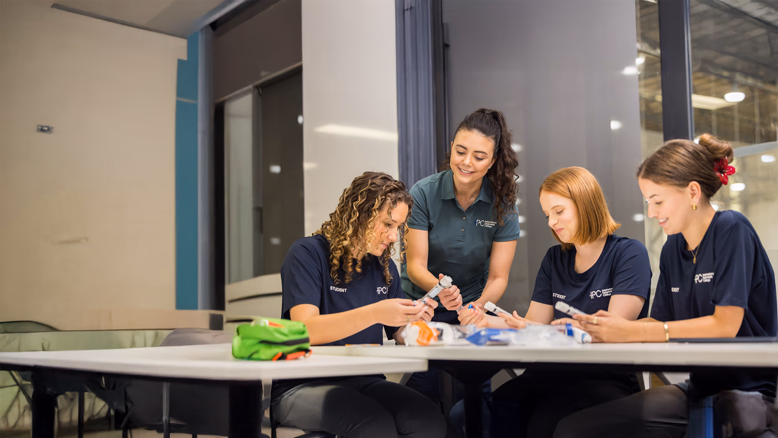 Instructor guiding two students as they practice assembling medical airway equipment during a hands-on training session in a classroom.