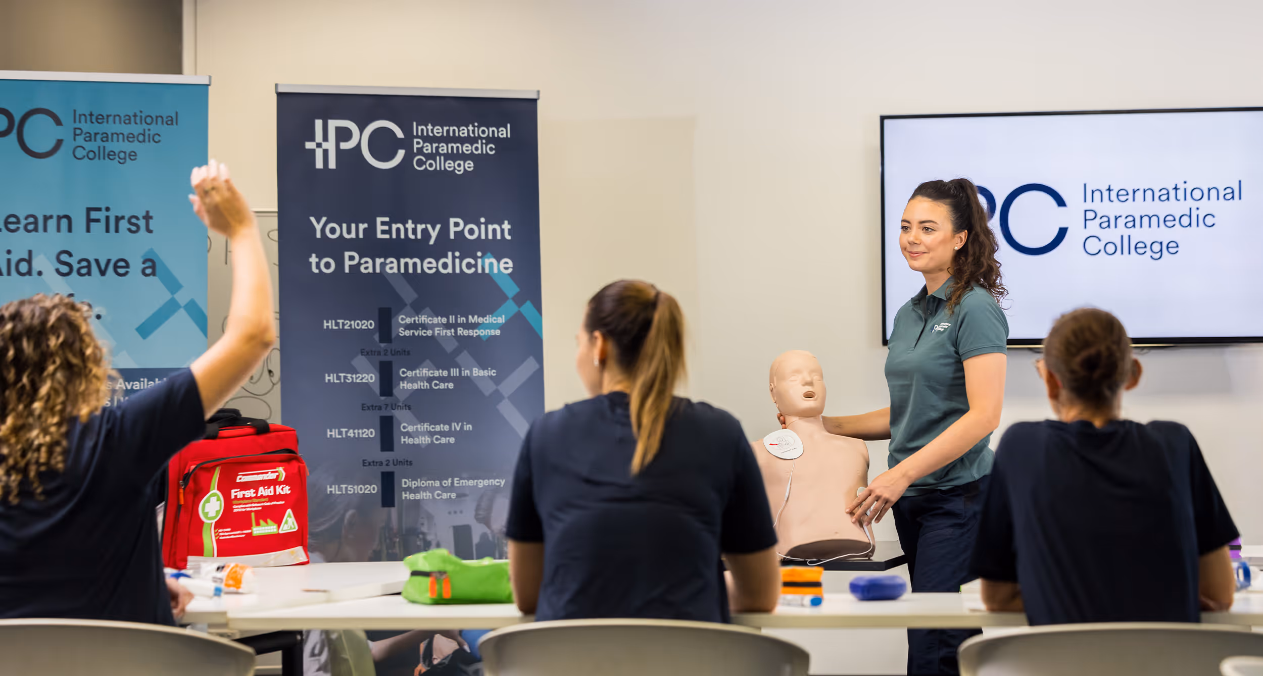 Instructor demonstrating CPR on a training mannequin in a classroom while students watch.