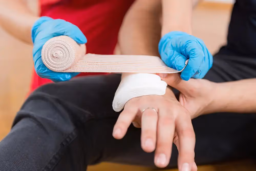 A person wearing blue medical gloves wraps an elastic bandage around another person’s injured wrist.
