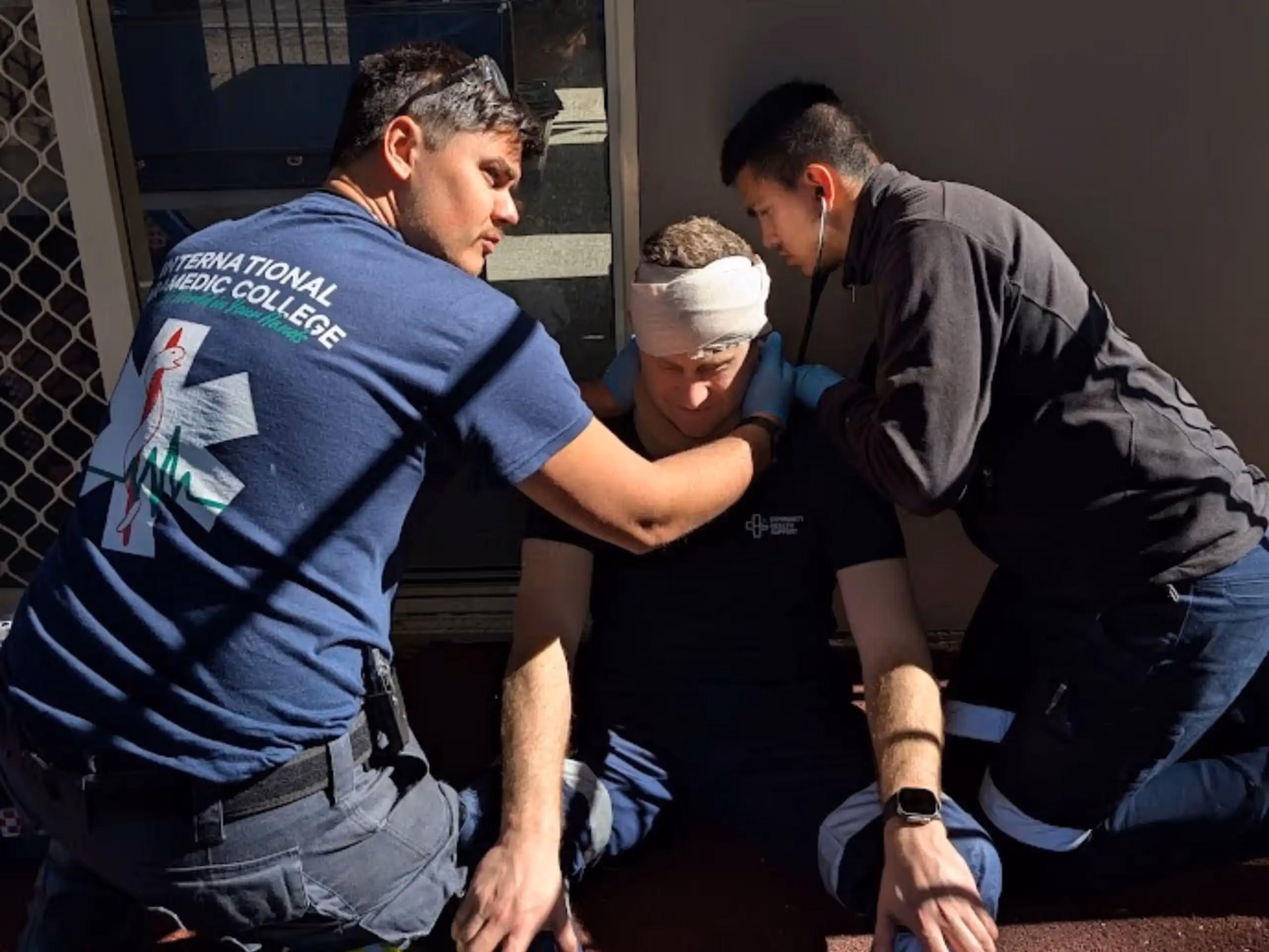 Paramedic trainees providing first aid to an injured person with a head bandage.