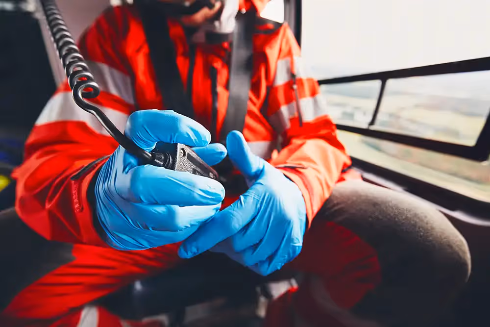 Paramedic wearing gloves using a radio inside an emergency helicopter.