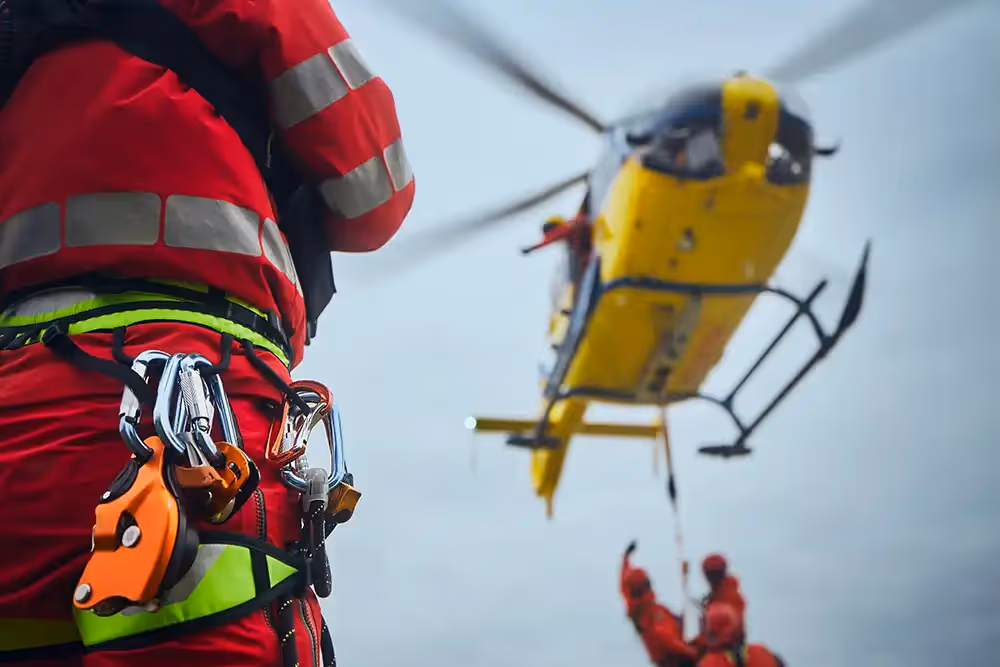 Rescue worker in safety gear assisting with a helicopter winch operation.