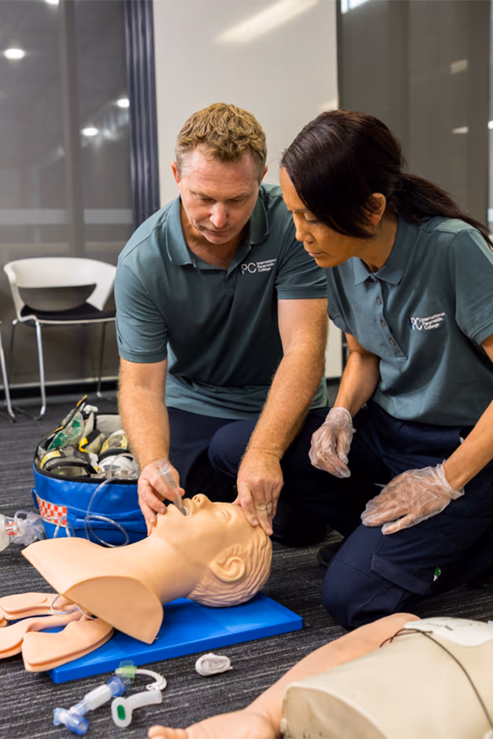 Two instructors practicing advanced airway management on a training mannequin, using medical equipment during a first aid training session.