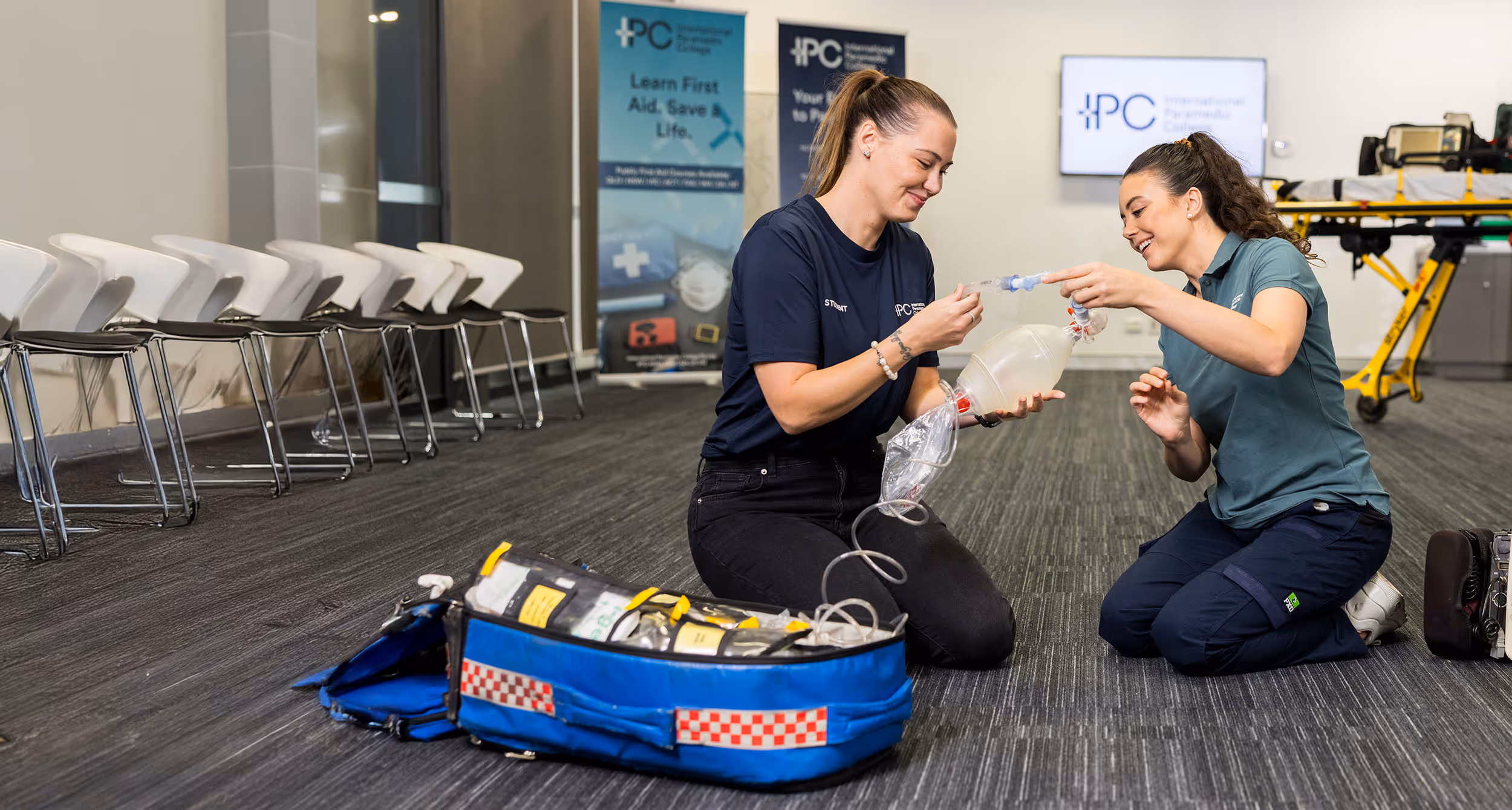 Instructor guiding a student as they practice using a bag-valve mask for ventilation during a hands-on first aid training session.