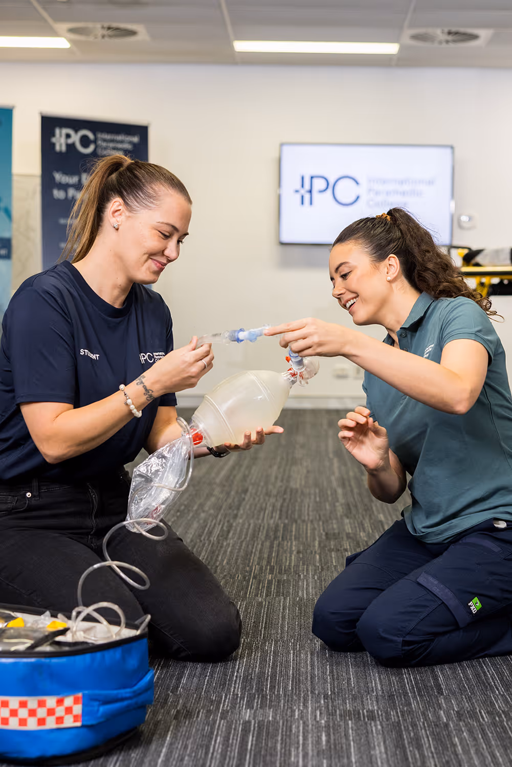 Instructor guiding a student as they practice using a bag-valve mask for ventilation during a hands-on first aid training session.