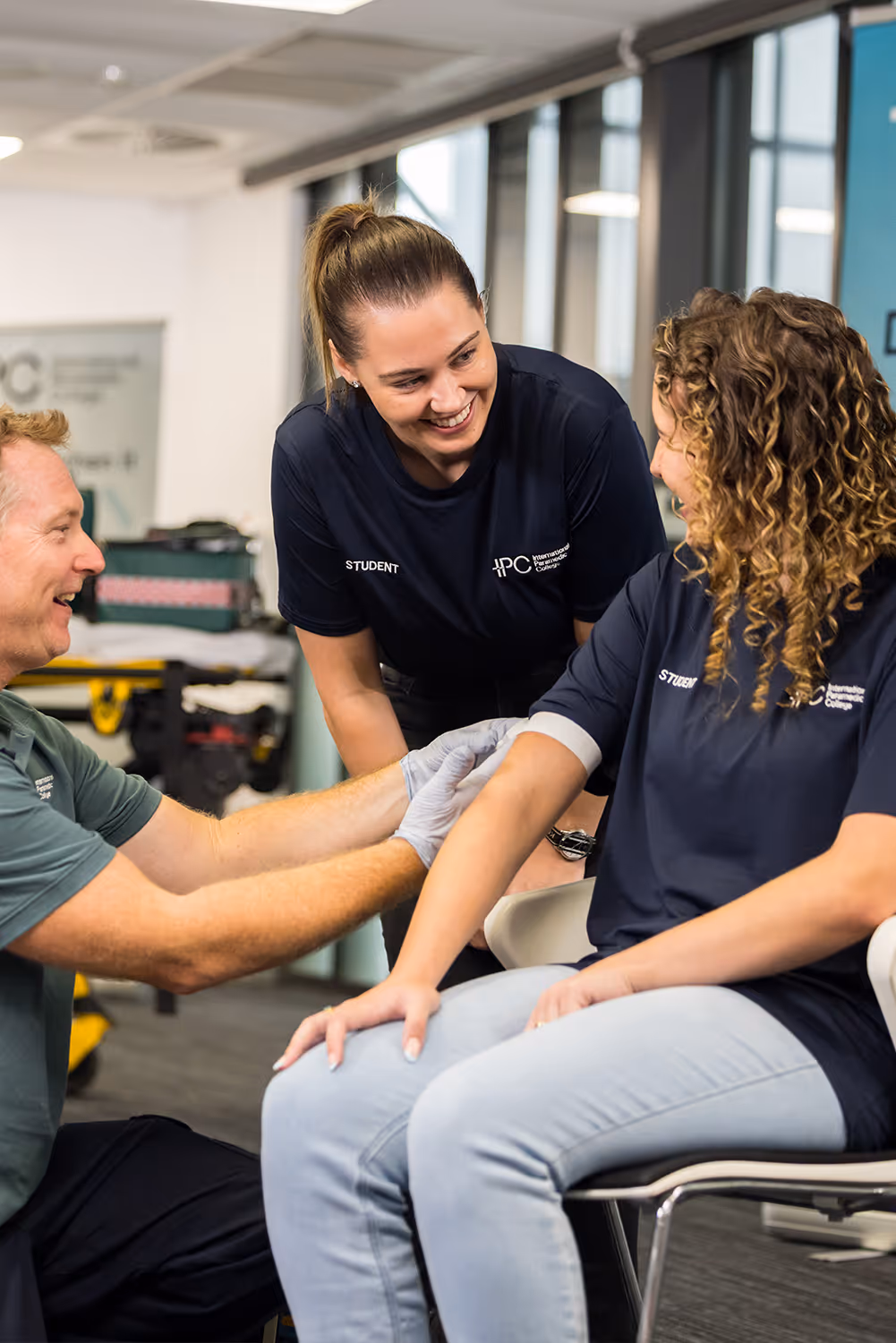 Instructor applying a bandage to a student’s arm while another student observes during a hands-on first aid training session.