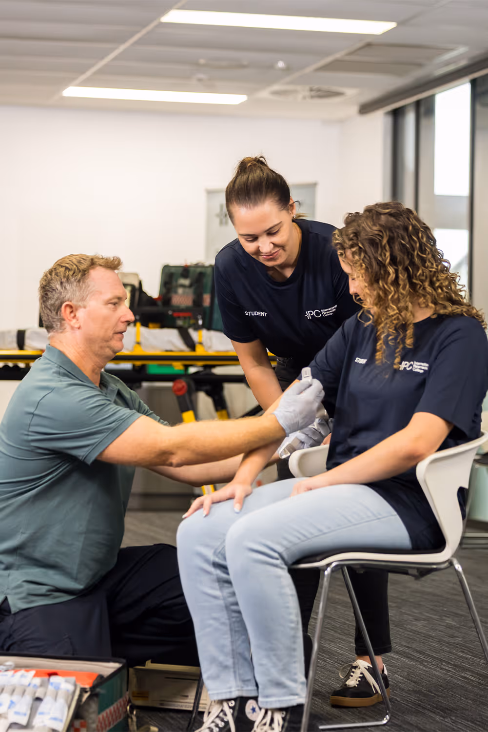 Instructor demonstrating how to apply a tourniquet to a student’s arm while another student observes during a first aid training session.