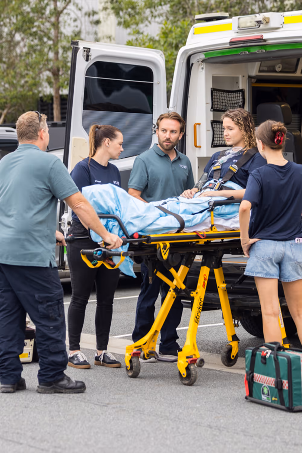 Paramedic students and an instructor transferring a patient on a stretcher into an ambulance during a practical training exercise.