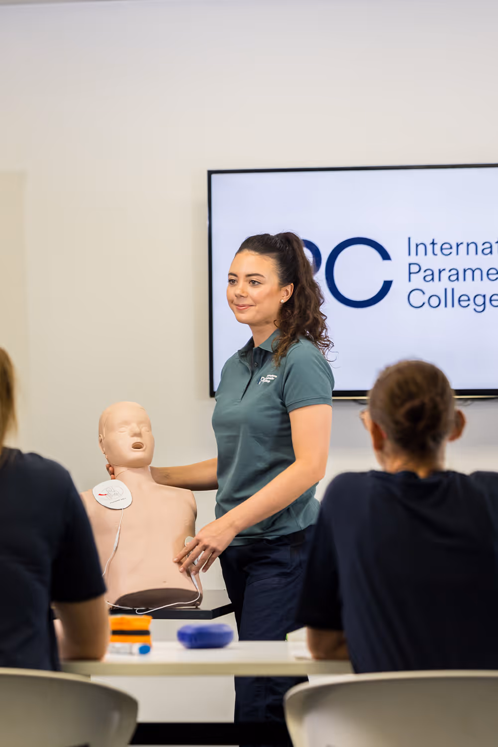 Paramedic instructor demonstrating CPR techniques on a training mannequin to students in a classroom setting.