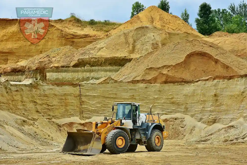 Front-end loader operating at a sand quarry with layered earth walls in the background.